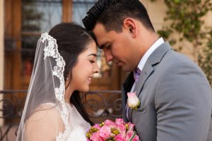 Profile view of a bridal couple touching each others' forehead in front of a church